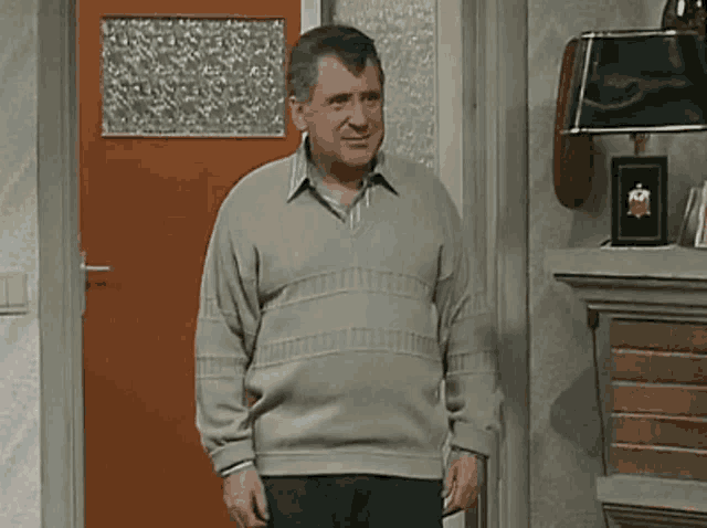 a man in a sweater is standing in front of an orange door