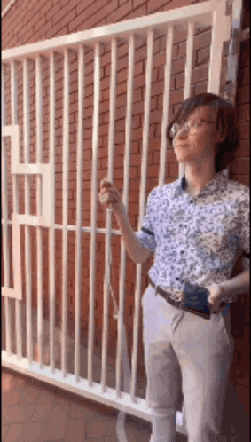 a woman with glasses is standing in front of a brick wall holding a cell phone .