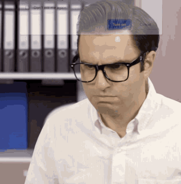 a man wearing glasses and a white shirt is looking at a screen that says " do n't ask me again "