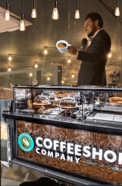 a man is holding a cup of coffee in front of a counter that says coffee shop company