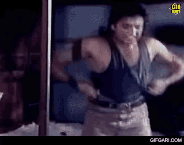 a man in a tank top is standing in front of a mirror and taking off his shirt .