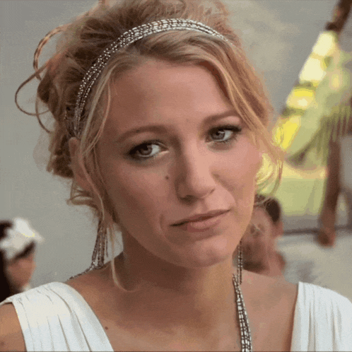 a woman wearing a white dress and a headband looks at the camera
