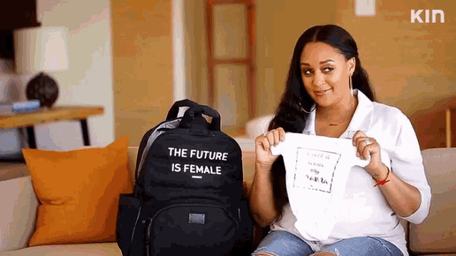 a woman is sitting on a couch holding a baby shirt and a backpack that says the future is female