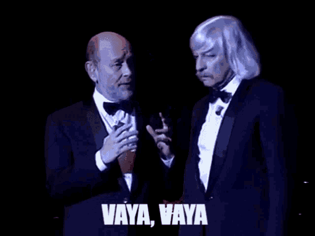 two men in tuxedos are standing next to each other on a stage and one of them is saying vaya vaya .
