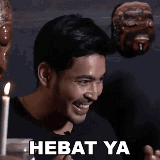 a man is sitting in front of a candle with the words hebat ya on his face
