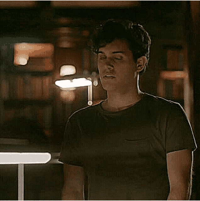 a man in a black t-shirt is standing in a dark room looking at something .