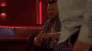 a man is sitting on a couch in a dark room with a woman standing behind him .