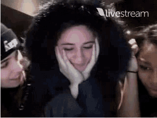 a woman wearing a fur hood is surrounded by two other women on a live stream .