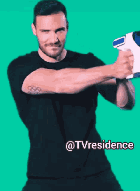 a man in a black shirt is holding a white object in front of a green background that says tvresidence