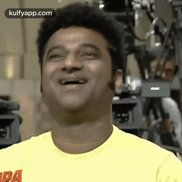 a man in a yellow shirt is laughing with his mouth open and his eyes closed .