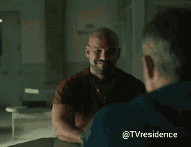 a man in a red shirt is talking to another man in a dark room with the hashtag @tvresidence