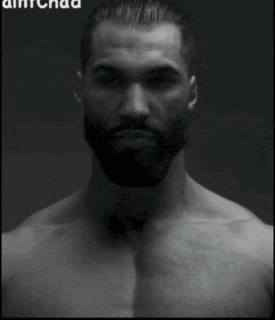 a black and white photo of a shirtless man with a beard sitting on a chair .