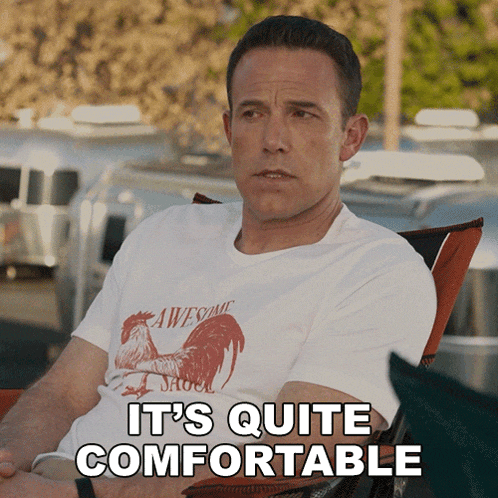 a man wearing an awesome rooster shirt is sitting in a chair