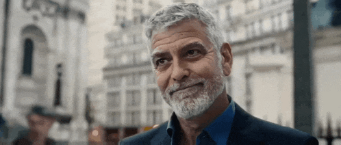 a man with gray hair and a beard is wearing a suit and blue shirt and looking up .