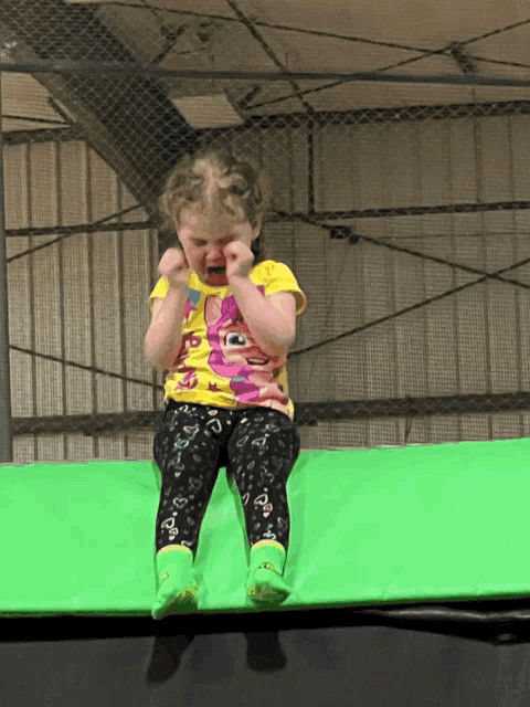 a little girl sitting on a green trampoline with a yellow shirt that says sesame street on it