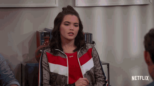 a woman in a red and white jacket is sitting in front of a netflix logo
