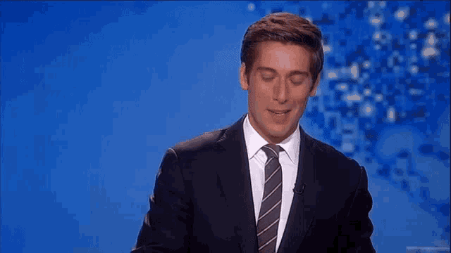 a man in a suit and tie stands in front of a blue screen