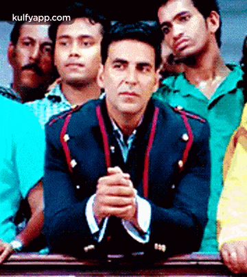 a man in a suit is sitting in front of a crowd of people with his hands folded .