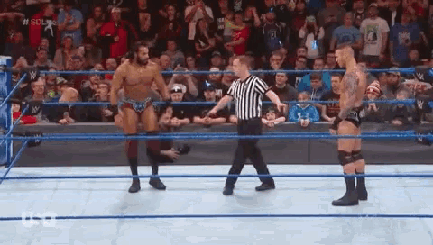 a referee is standing in the middle of a wrestling ring between two men .