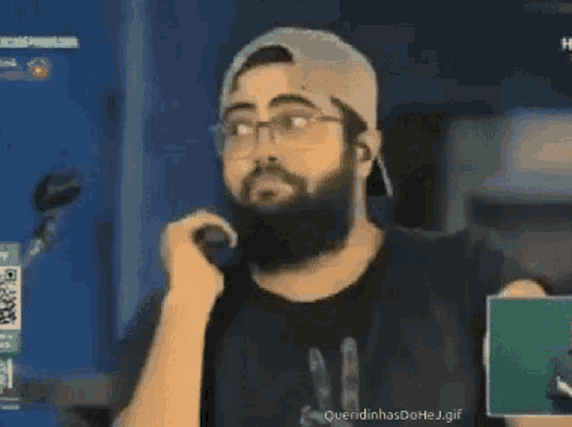 a man with a beard is talking into a microphone while wearing glasses and a hat .