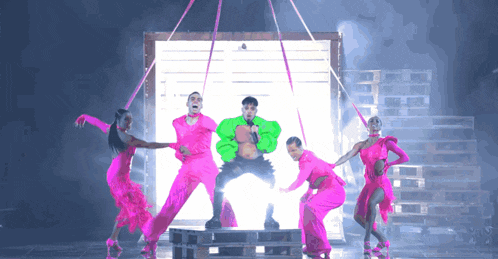 a man in a green sweater is surrounded by pink dancers