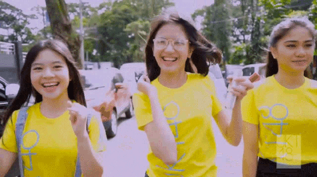 three girls wearing yellow shirts with the letter o on them are walking down a street