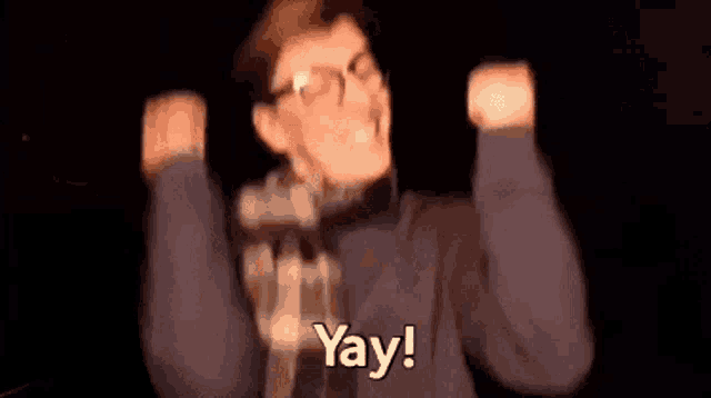 a man wearing glasses is raising his arms in the air and saying `` yay '' .