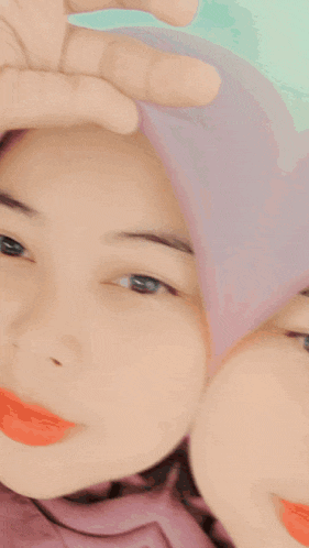 a woman wearing a pink striped shirt and a purple hijab is making a heart with her hands