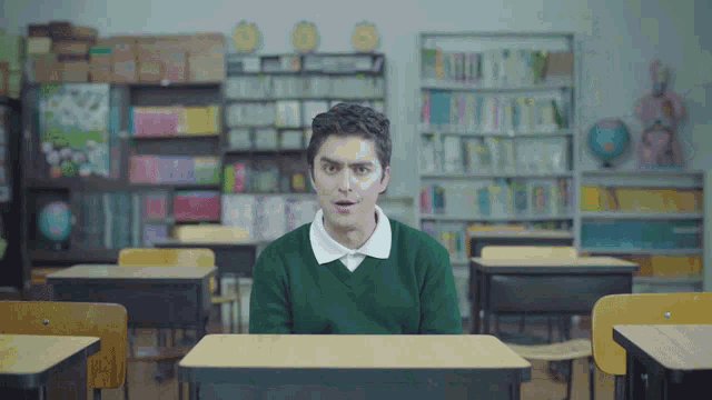 a man in a green sweater sits at a desk in a library