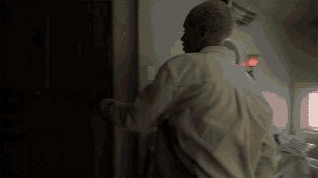a man in a white shirt is opening a door to a dark room