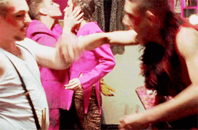 a woman in a pink jacket kisses a man in a white tank top