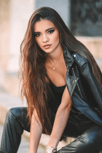 a woman with long hair is wearing a black leather jacket and black pants