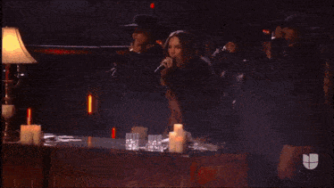 a woman singing into a microphone with a lamp and candles in the background