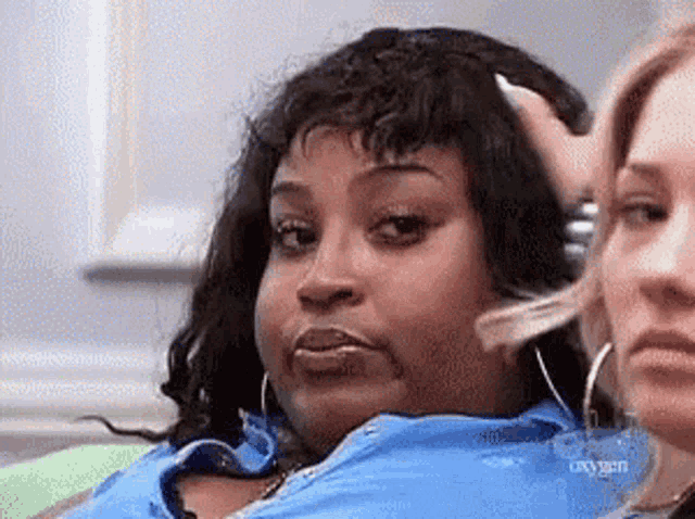 a woman is sitting on a couch with her hand on her head and another woman is sitting next to her .