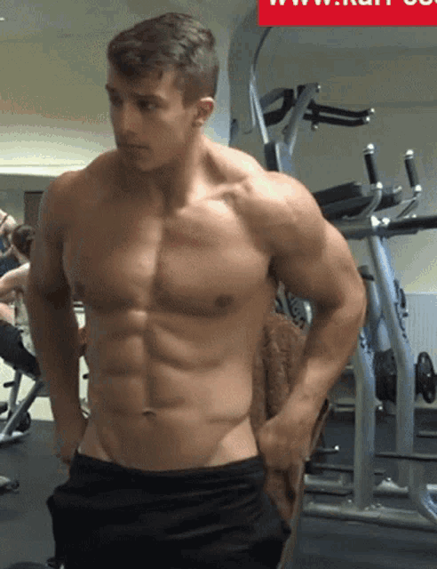 a shirtless man is standing in a gym with a red sign that says www
