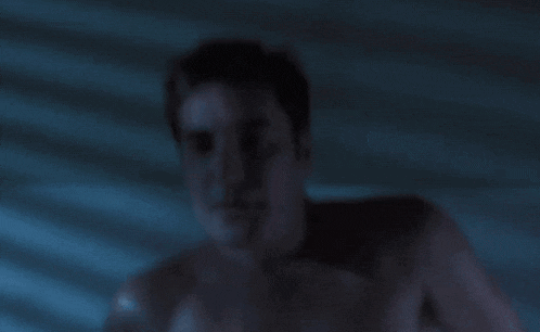 a man without a shirt is laying in a dark room