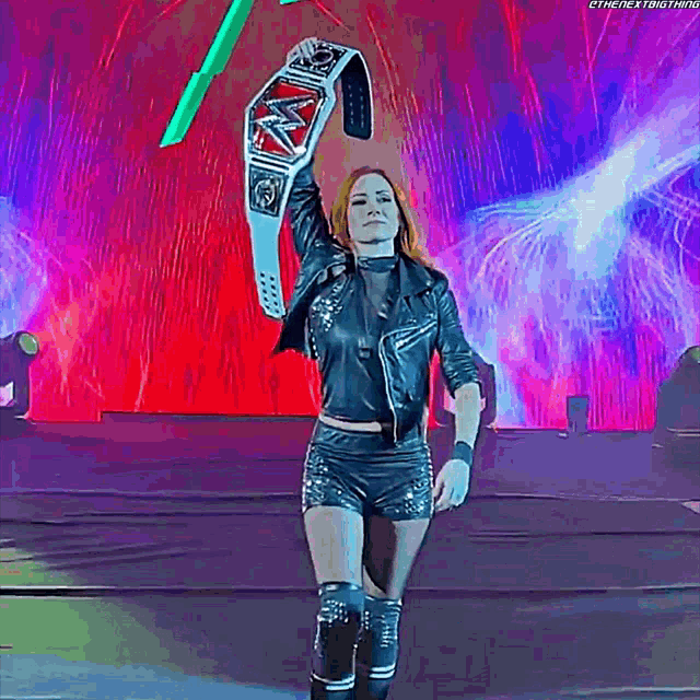 a woman in a leather jacket is holding a wrestling championship belt over her head .