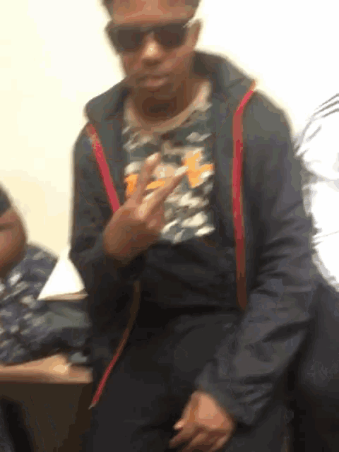a man wearing sunglasses and a black jacket is giving a middle finger