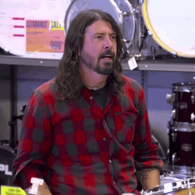 a man with long hair and a beard is playing a drum set in front of a sign that says clearance sale