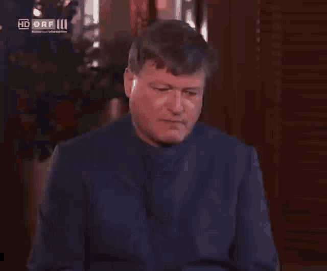 a man in a blue jacket holds his hand to his forehead in front of a hd orf logo