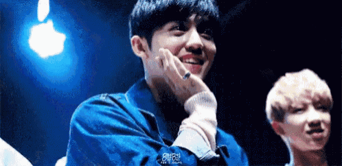 a young man in a blue jacket is smiling with his hand on his face .