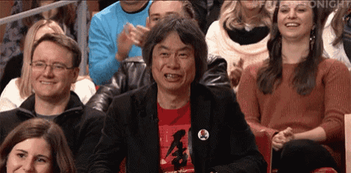 a man wearing a red shirt with chinese writing on it is sitting in a crowd of people applauding .