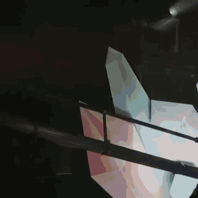 a pink and green paper airplane is flying through the air in a dark room