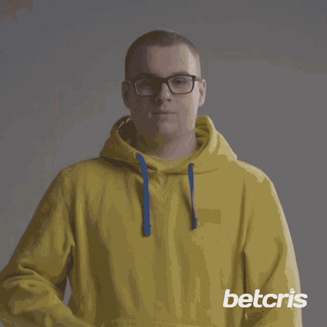 a man wearing glasses and a yellow hoodie is giving the ok sign