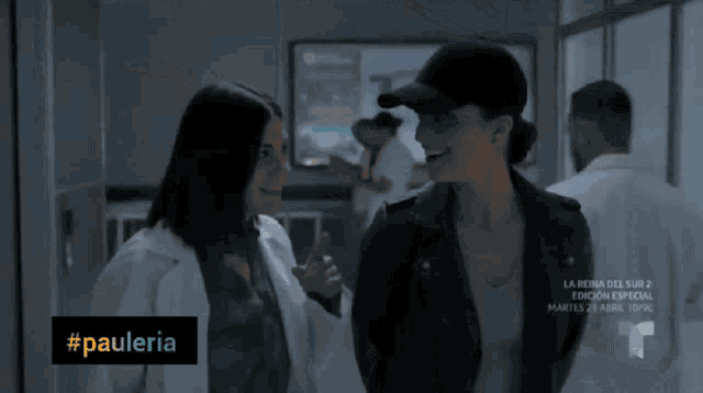 two women are standing next to each other in a hallway with a sign that says #pauleria on it