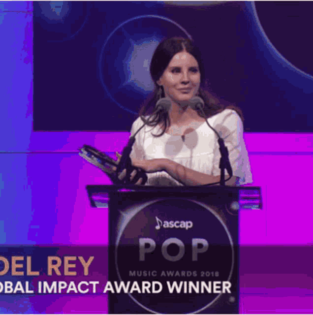 a woman stands behind a podium that says pop music awards