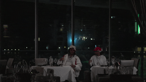 two men sit at a table with wine glasses in front of a large window