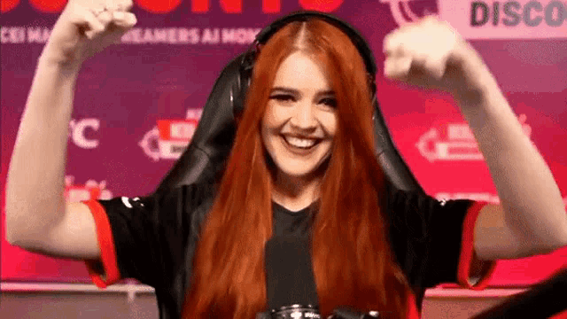 a woman with red hair is wearing headphones and smiling while sitting in a gaming chair .