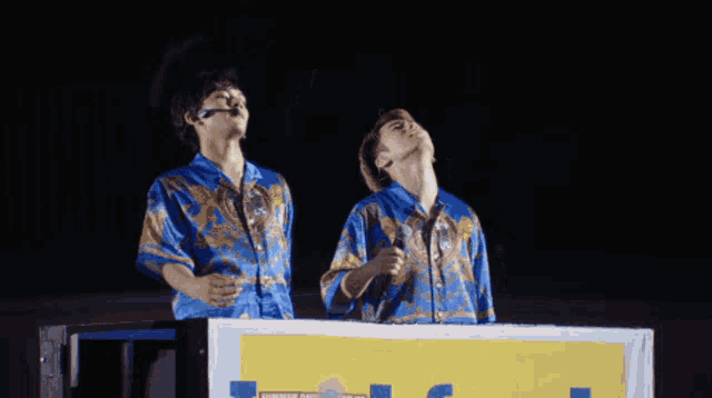 two men standing in front of a sign that says ' hawaiian aloha ' on it