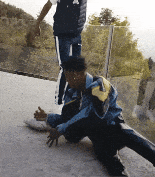 a man in a blue jacket is kneeling on the ground while another man stands behind him